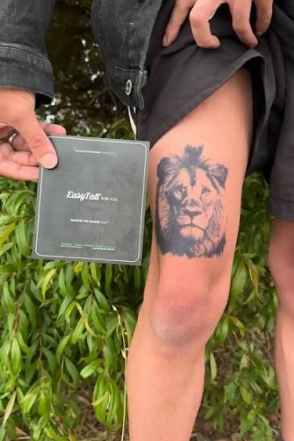 Are temporary tattoos safe? Hand holding a dark EasyTatt card beside a black lion face temporary tattoo on a thigh