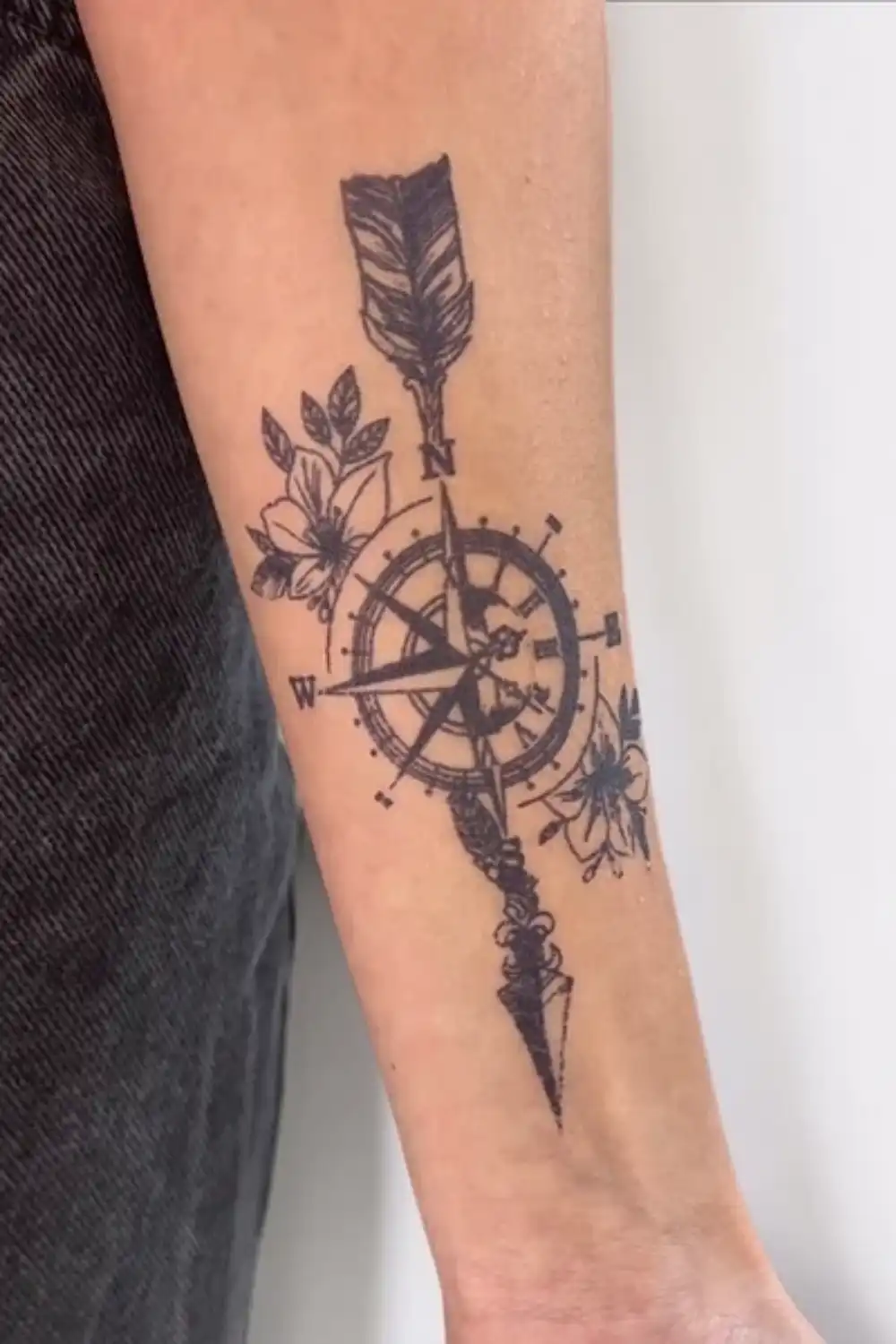 An EasyTatt temporary tattoo on an arm showing a detailed compass and arrow surrounded by delicate floral patterns